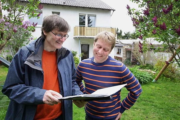 Energieberater mit Mappe voller Unterlagen und Kunde im Gespräch im Garten eines Wohngebäudes
